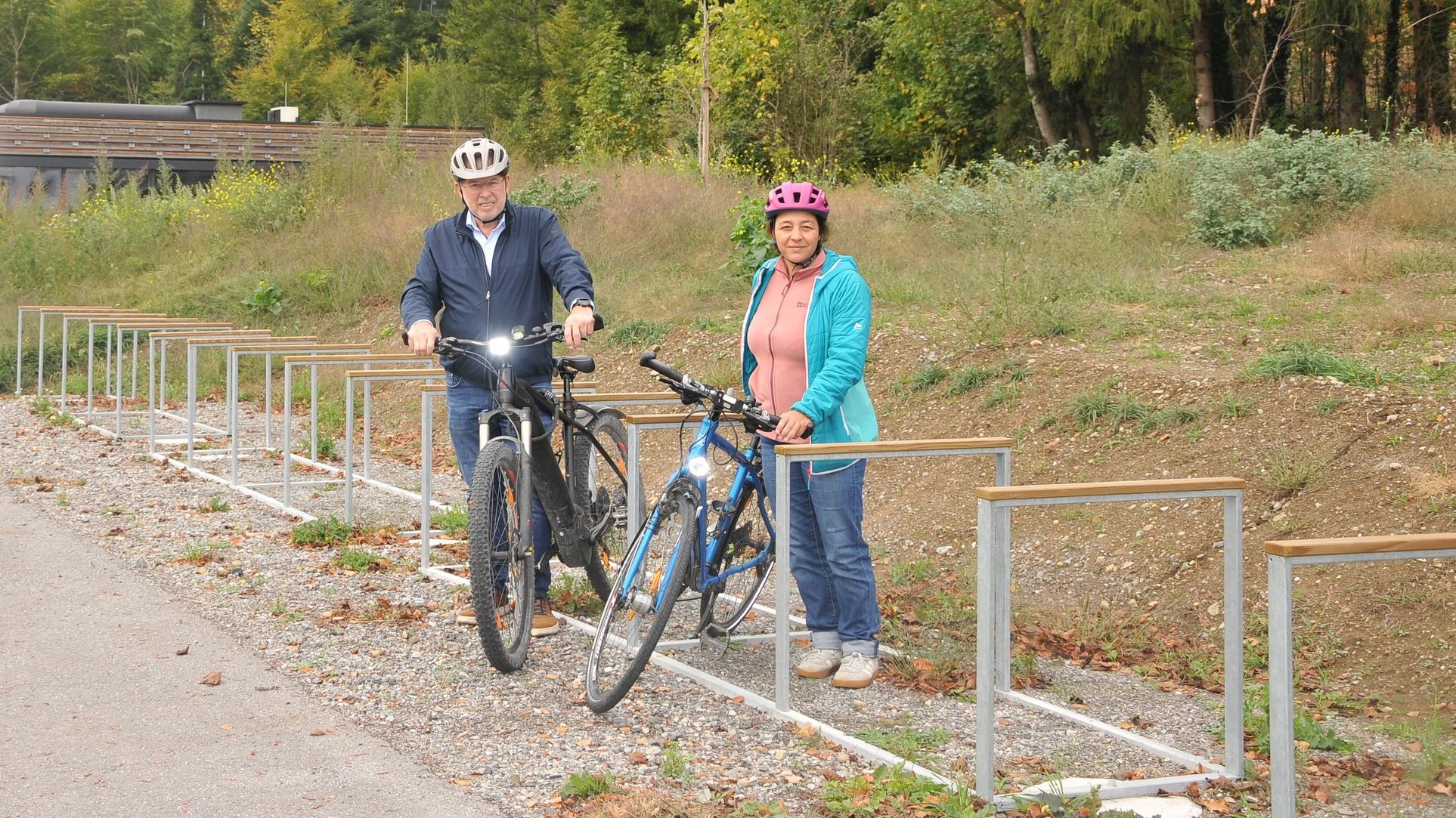 Zwei Radfahrer mit Helmen stehen neben ihren Fahrrädern auf einem Radabstellplatz