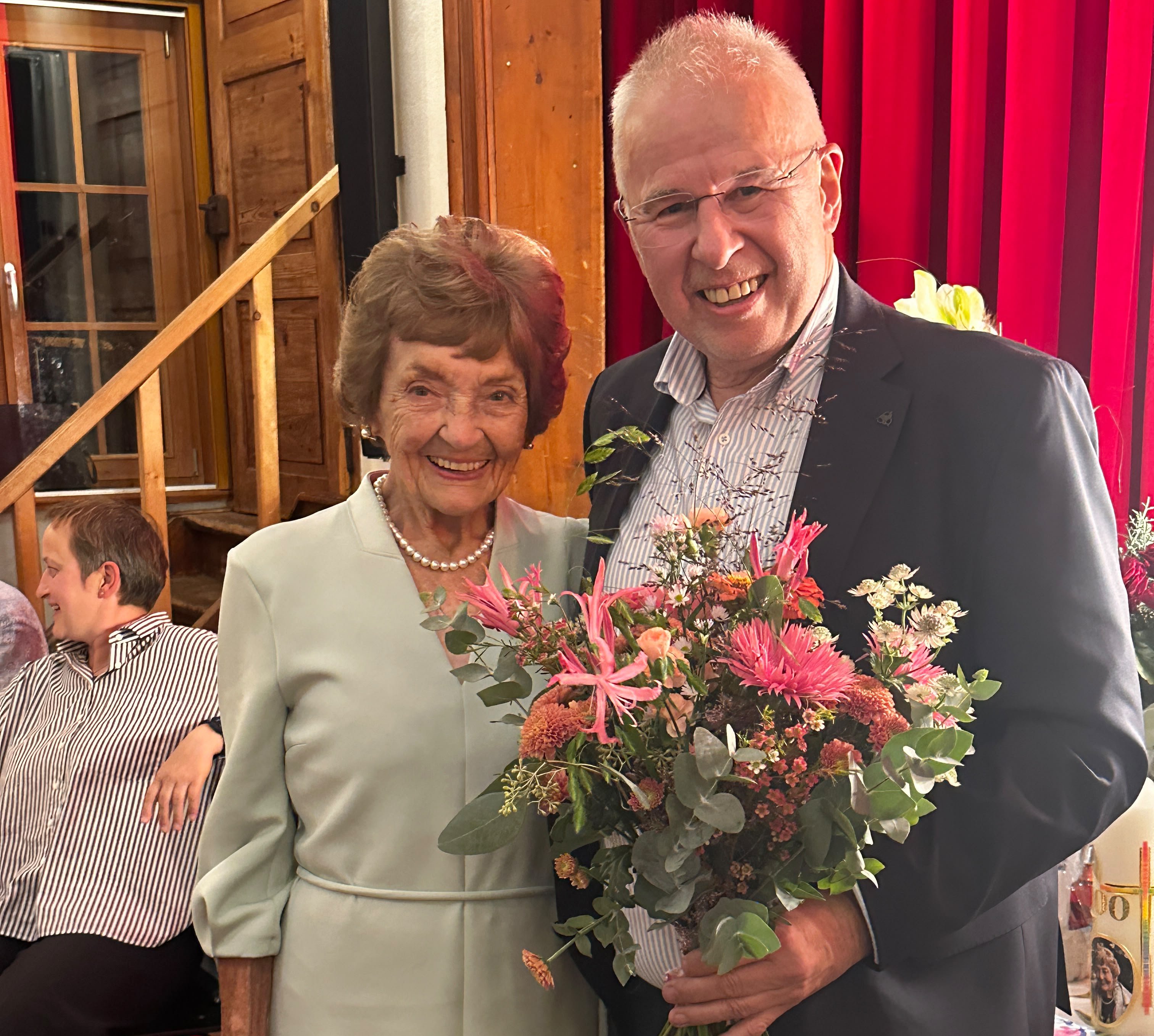 Ältere Frau mit Perlenkette und Mann mit Blumenstrauß lächeln in Österreich