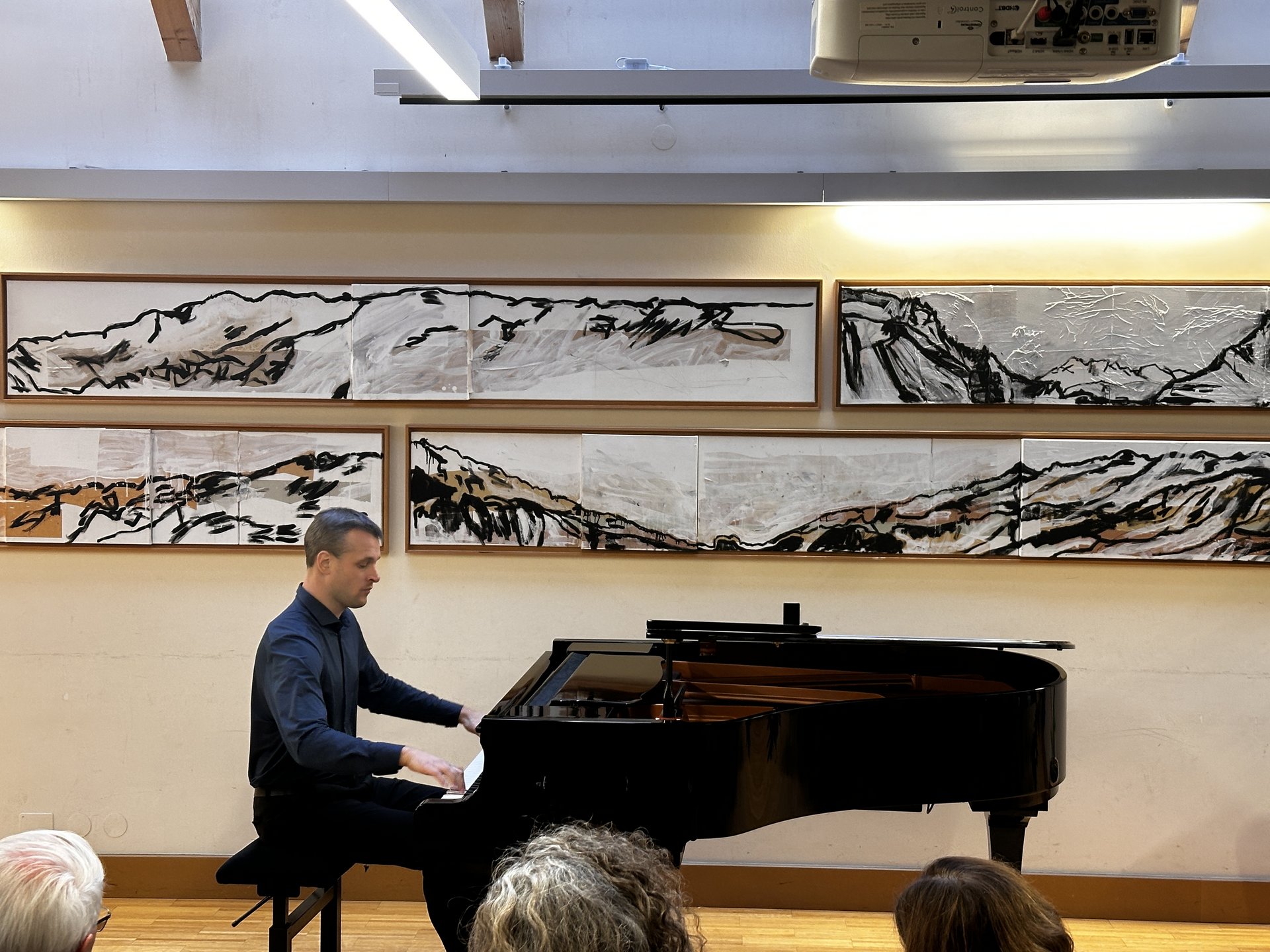 Pianist spielt Konzertflügel vor Berglandschaft-Gemälden im Festsaal